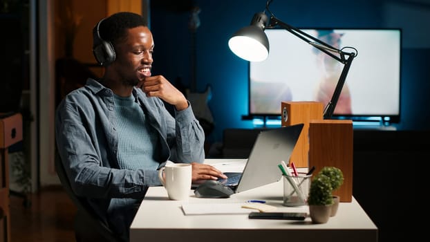 Young focused freelancer attending an online meeting from his home office, discussing with associates remotely. Smiling black man engages in virtual communication, remote technology. Camera B.