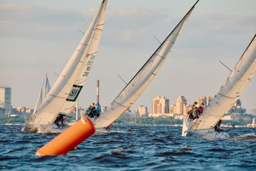 Russia, St.Petersburg, 07 June 2024: Sailing regatta in the Gulf of Finland at sunset, hot race of several yachts, teamwork, yachtsmen sitting on board the boat. High quality photo