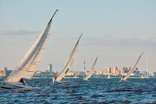 Russia, St.Petersburg, 07 June 2024: Sailing regatta in the Gulf of Finland at sunset, hot race of several yachts, teamwork, yachtsmen sitting on board the boat. High quality photo