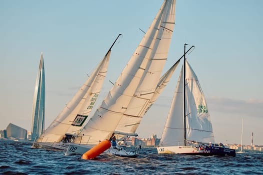 Russia, St.Petersburg, 07 June 2024: Sailing regatta in the Gulf of Finland at sunset, hot race of several yachts, teamwork, yachtsmen sitting on board the boat. High quality photo