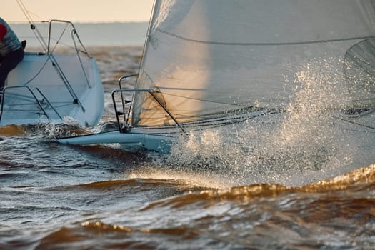 Sailing regatta in the Gulf of Finland at sunset, the bows of two sailing yachts competing in a race, splashing water from under the boats, teamwork, board the boat. High quality photo