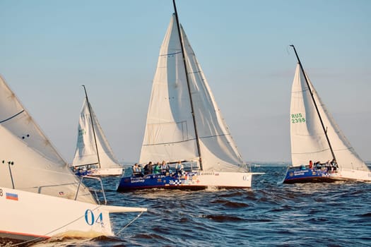 Russia, St.Petersburg, 07 June 2024: Sailing regatta in the Gulf of Finland at sunset, hot race of several yachts, teamwork, yachtsmen sitting on board the boat. High quality photo