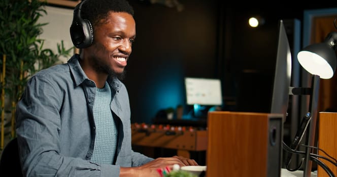 Black guy video editor working with dual monitors for creative content, editing video footage and does color grading for the media creation. Male professional works in post production. Camera A.