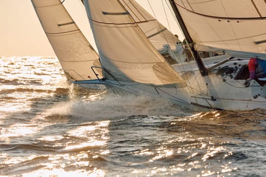 Sailing regatta in the Gulf of Finland at sunset, the bows of two sailing yachts competing in a race, splashing water from under the boats, teamwork, board the boat. High quality photo