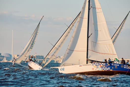 Russia, St.Petersburg, 07 June 2024: Sailing regatta in the Gulf of Finland at sunset, hot race of several yachts, teamwork, yachtsmen sitting on board the boat. High quality photo