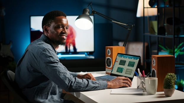 Black accountant working on monthly revenue balance on laptop at home, calculating investment money to double the profit. Economist looks into legal trade statistics, supply and demand. Camera B.