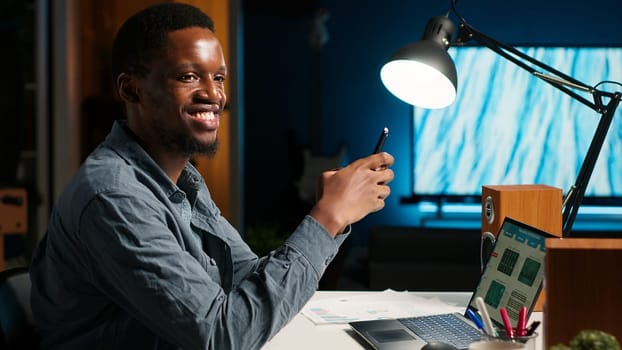 Independent adult teleworking from home and using his mobile phone, navigating social media and answering emails before starting his daily tasks completion. Comfortable modern setup. Camera B.