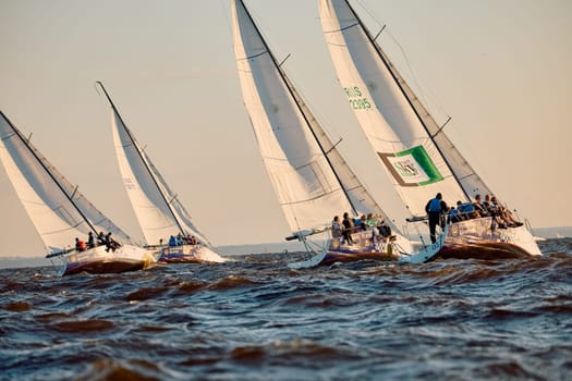 Russia, St.Petersburg, 07 June 2024: Sailing regatta in the Gulf of Finland at sunset, hot race of several yachts, teamwork, yachtsmen sitting on board the boat. High quality photo