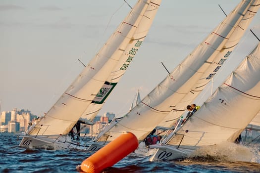 Russia, St.Petersburg, 07 June 2024: Sailing regatta in the Gulf of Finland at sunset, hot race of several yachts, teamwork, yachtsmen sitting on board the boat. High quality photo