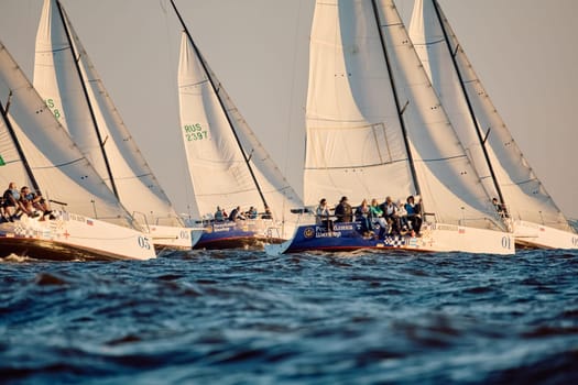Russia, St.Petersburg, 07 June 2024: Sailing regatta in the Gulf of Finland at sunset, hot race of several yachts, teamwork, yachtsmen sitting on board the boat. High quality photo
