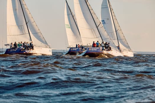 Russia, St.Petersburg, 07 June 2024: Sailing regatta in the Gulf of Finland at sunset, hot race of several yachts, teamwork, yachtsmen sitting on board the boat. High quality photo