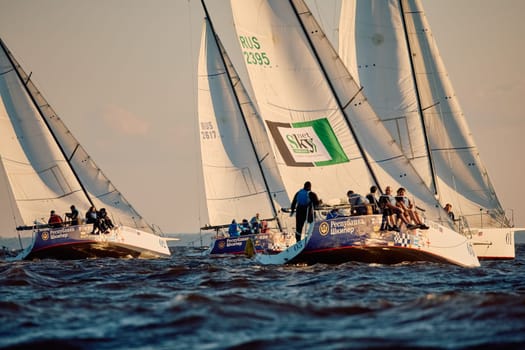 Russia, St.Petersburg, 07 June 2024: Sailing regatta in the Gulf of Finland at sunset, hot race of several yachts, teamwork, yachtsmen sitting on board the boat. High quality photo