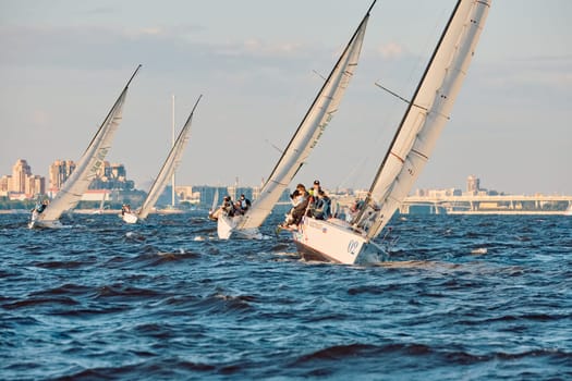 Russia, St.Petersburg, 07 June 2024: Sailing regatta in the Gulf of Finland at sunset, hot race of several yachts, teamwork, yachtsmen sitting on board the boat. High quality photo