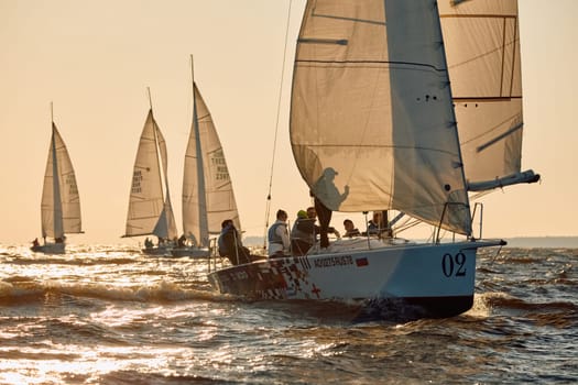 Russia, St.Petersburg, 07 June 2024: Sailing regatta in the Gulf of Finland at sunset, hot race of several yachts, teamwork, yachtsmen sitting on board the boat. High quality photo
