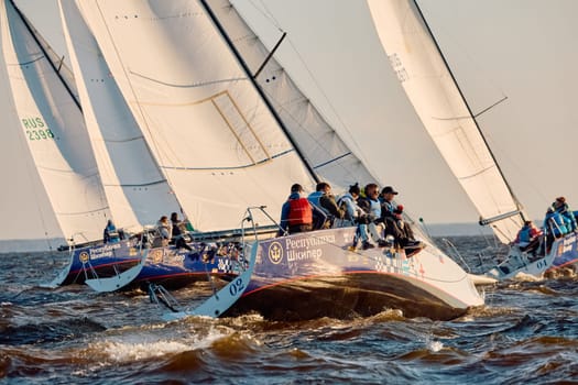Russia, St.Petersburg, 07 June 2024: Sailing regatta in the Gulf of Finland at sunset, hot race of several yachts, teamwork, yachtsmen sitting on board the boat. High quality photo