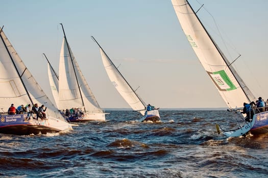 Russia, St.Petersburg, 07 June 2024: Sailing regatta in the Gulf of Finland at sunset, hot race of several yachts, teamwork, yachtsmen sitting on board the boat. High quality photo