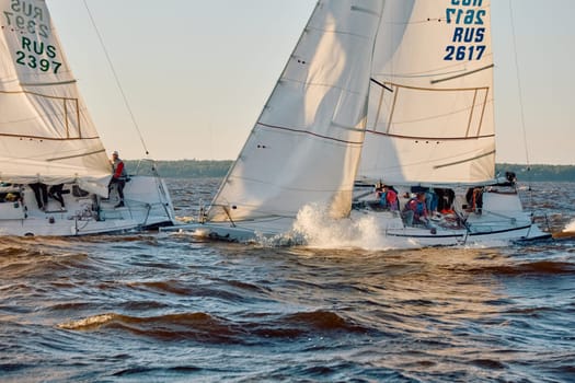 Russia, St.Petersburg, 07 June 2024: Sailing regatta in the Gulf of Finland at sunset, hot race of several yachts, teamwork, yachtsmen sitting on board the boat. High quality photo