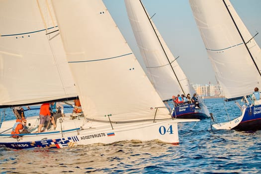 Russia, St.Petersburg, 24 May 2024: Sailing regatta in the Gulf of Finland at sunset, hot race of several yachts, teamwork, yachtsmen sitting on board the boat. High quality photo