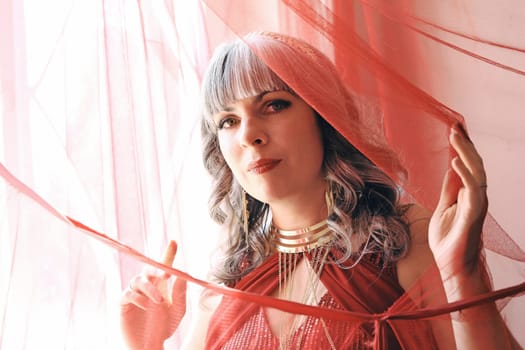 A pretty woman in a red dress looks through a curtain