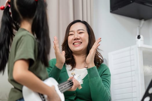 A mother expresses joy and encouragement as her daughter plays the ukulele, highlighting the importance of music in family bonding.