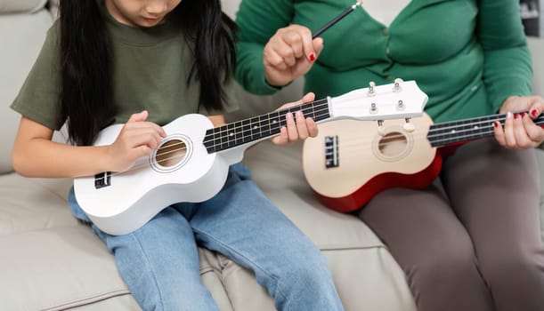 A mother patiently guides her daughter in learning the ukulele, emphasizing the importance of music education and family bonding.