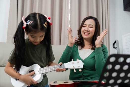 A young girl enthusiastically learns to play the ukulele with her mothers encouragement, highlighting the joy of music education in a nurturing environment.