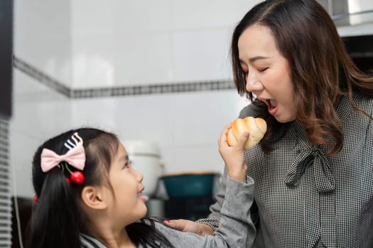 A little girl playfully offers a pastry to her mother, creating a joyful and engaging moment in the kitchen.