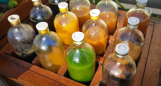 Colorful Bottles of traditional natural organic medicine locally called jamu, Displayed in Wooden Case on a Sunny Day, Various colorful bottles filled with liquids arranged in a wooden container outdoors under sunlight.