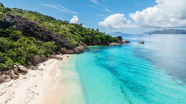 A tranquil beach with vibrant turquoise water and soft white sand surrounded by lush greenery. Curieuse, Seychelles.