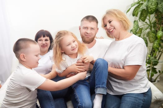 A joyful family engages in playful activities indoors, wearing matching casual outfits and sharing laughter together on a cozy couch.