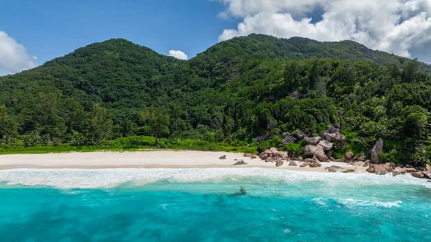 Dense green tropical forest next to a secluded beach with calm blue waters. La Digue, Seychelles.