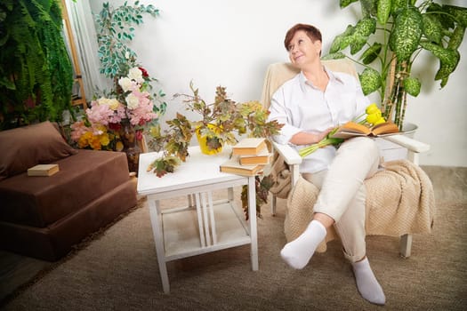 A middle-aged woman relaxes in a cozy room, surrounded by flowers and enjoying a book on International Women's Day.
