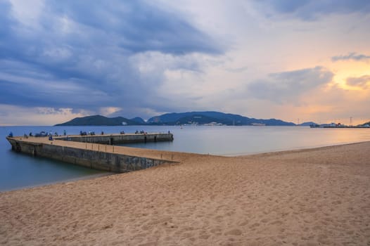 Pier with fishermen in sea at sandy beach at sunrise in the morning. View of Vinpearl Island in Nha Trang in Vietnam. Long exposure landscape
