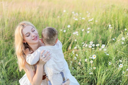 Mom hugs little child in a meadow with daisies, cute mom and two-year-old child have fun in a summer field. High quality photo