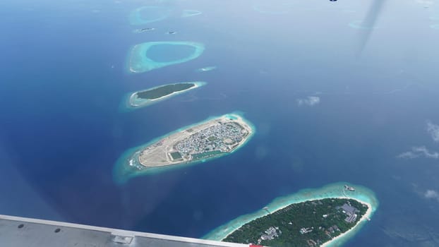 Airplane passenger enjoying the breathtaking view of the maldives islands, a tropical paradise with crystal-clear turquoise waters and lush green vegetation