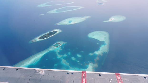 Airplane wing flying over the maldives islands and atolls, showing the beautiful turquoise water and white sand beaches of this tropical paradise in the indian ocean