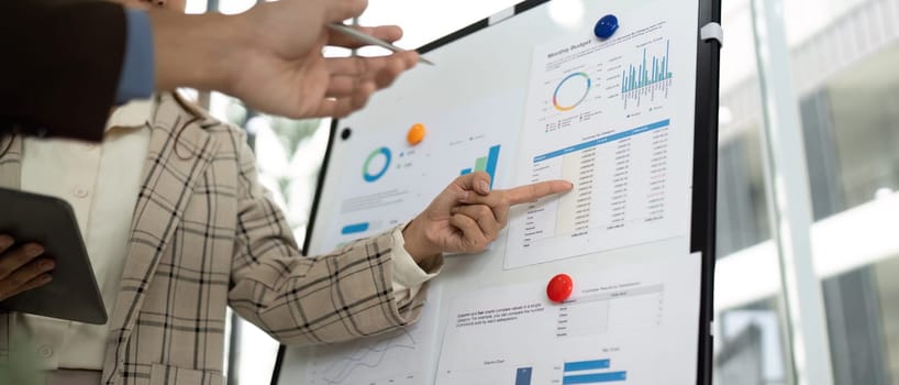 A close-up of a businesswoman pointing at data metrics while discussing with a colleague in a bright office environment.