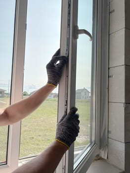 A worker adjusts a plastic window in a new country house. Installing plastic windows in a new building. Construction and renovation concept.