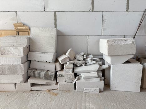 The remains of white building blocks are stacked against a wall at a construction site. Disposal of construction waste.