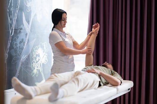 Therapist Performing Arm Stretch. A female therapist performs an arm stretch technique on a male patient lying on a treatment bed.