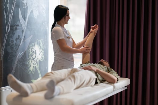 Therapist Performing Arm Stretch. A female therapist performs an arm stretch technique on a male patient lying on a treatment bed.