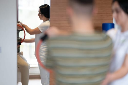 A male patient performing arm exercises using a resistance ring under supervision during a rehabilitation session.