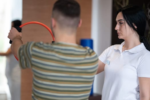 A male patient performing arm exercises using a resistance ring under supervision during a rehabilitation session.