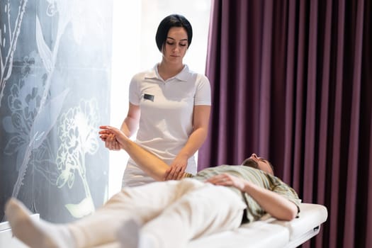 Therapist Performing Arm Stretch. A female therapist performs an arm stretch technique on a male patient lying on a treatment bed.