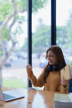 A cheerful young woman celebrates with a fist pump at her desk studying..