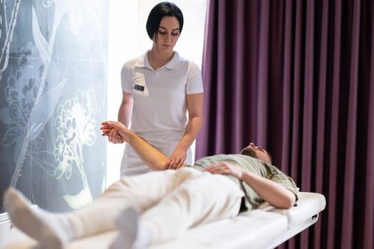 Therapist Performing Arm Stretch. A female therapist performs an arm stretch technique on a male patient lying on a treatment bed.