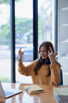 Young woman cheerfully making rock and roll hand gestures at her desk..