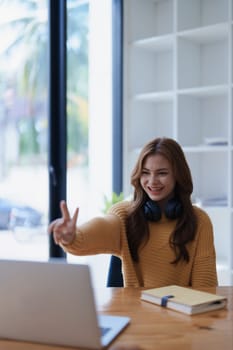 A young woman cheerfully waves during a video call on her laptop at home..