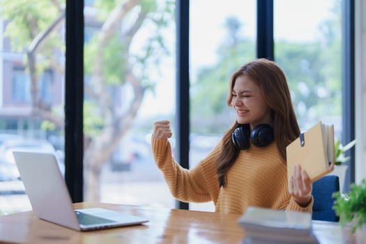 An excited woman celebrates success while working from home with laptop..