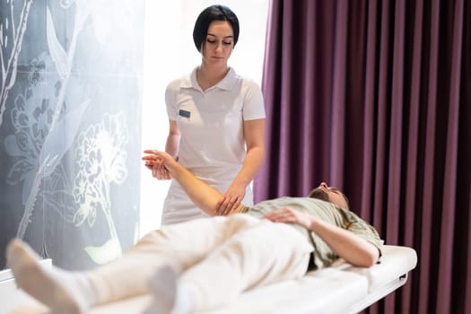 Therapist Performing Arm Stretch. A female therapist performs an arm stretch technique on a male patient lying on a treatment bed.